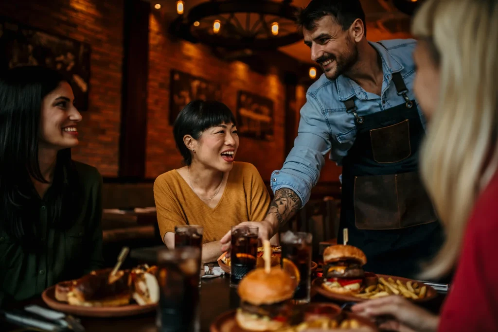 Friendly waiter serving meals to smiling customers, illustrating how marketing services for restaurants help boost foot traffic and loyalty.