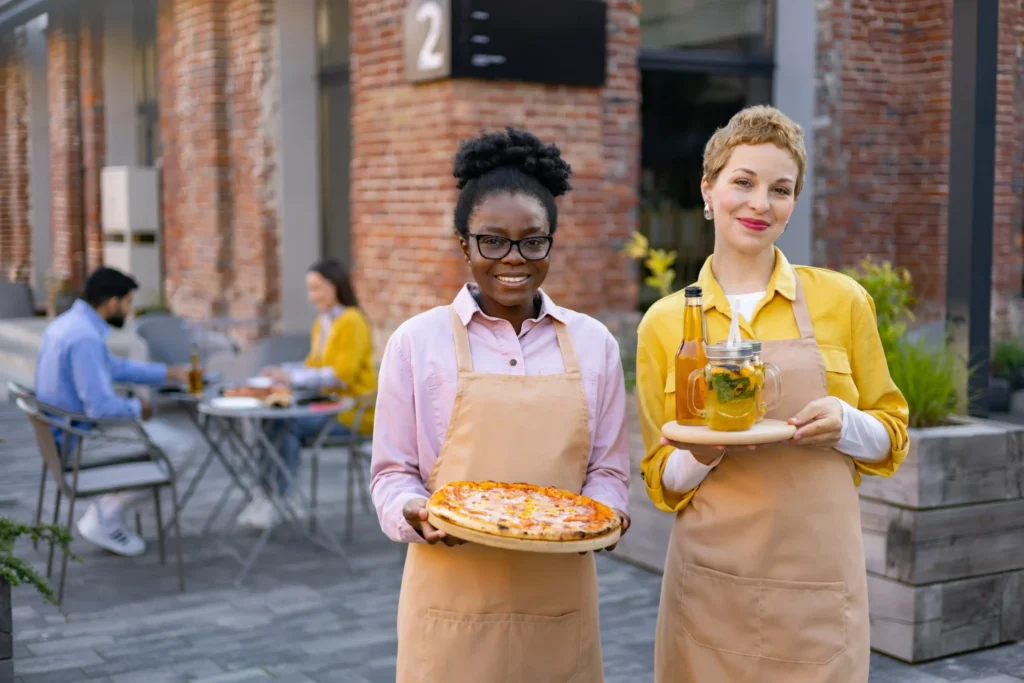 Restaurant staff serving pizza and drinks outdoors, showcasing hospitality and teamwork in pizza marketing ideas.