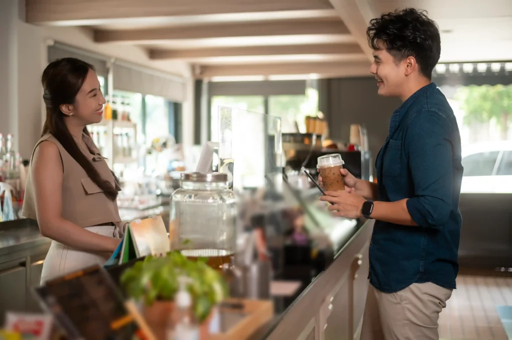 Friendly barista chatting with a customer ordering iced coffee at the counter, symbolizing engaging cafe promotion ideas for loyalty.