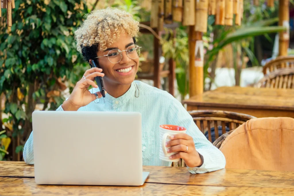 Woman smiling while taking a client call and working on a laptop outdoors, representing freelance digital marketing services and remote collaboration.