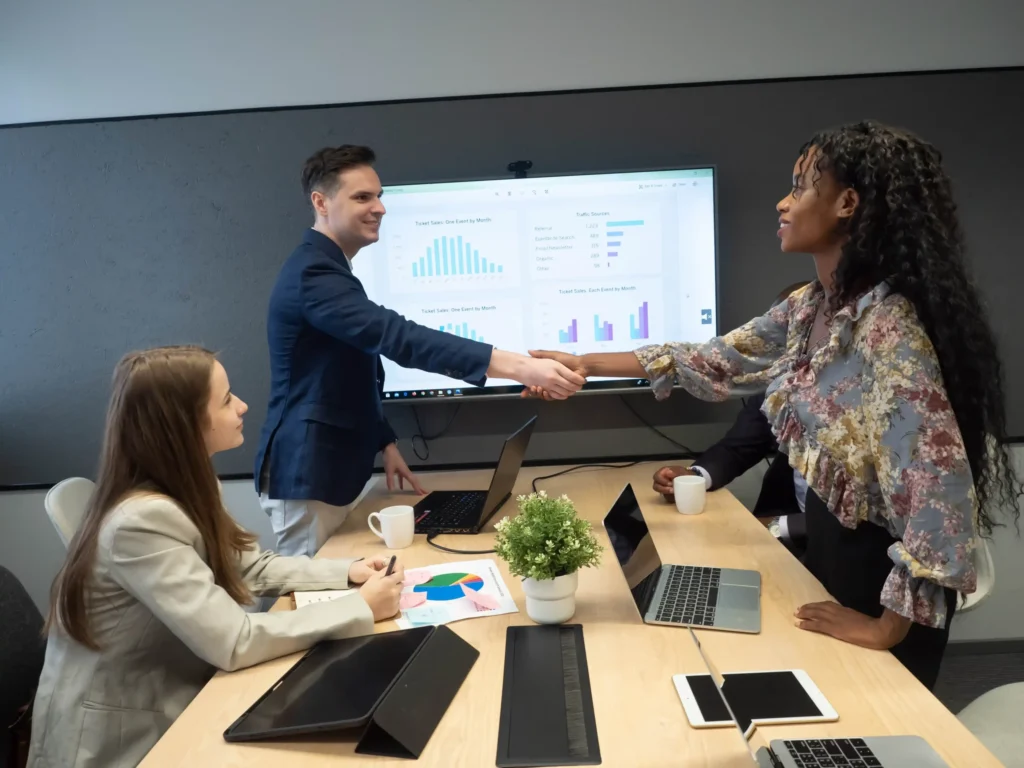A business owner and marketing consultant shake hands while reviewing analytics, symbolizing partnership in local search marketing services.
