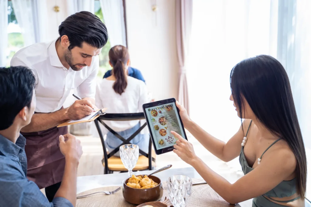 Digital marketing for restaurant success shown through a server taking orders while customers browse a digital menu in a modern dining space