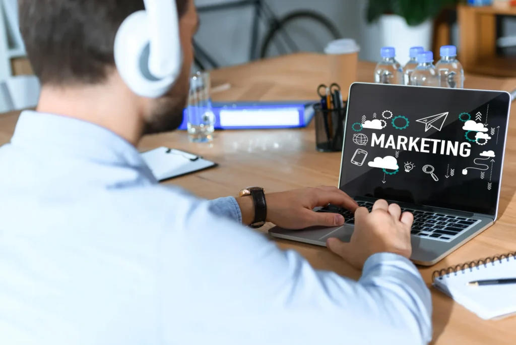 Man wearing headphones working on a laptop displaying marketing graphics, representing internet marketing services in a modern workspace.