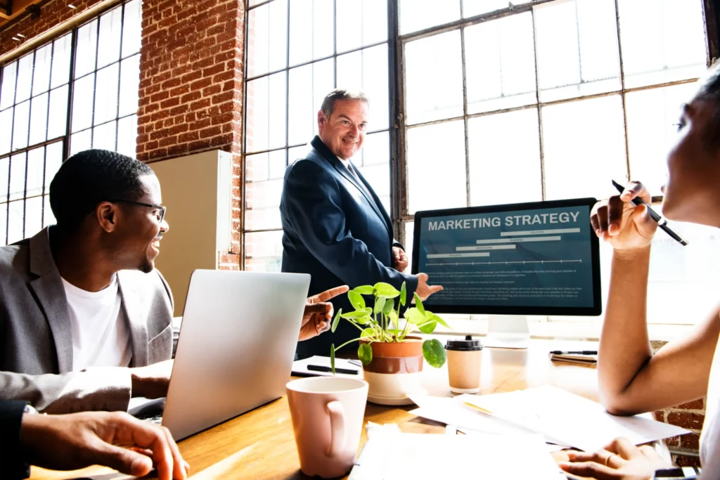 A marketing expert presents a strategy on a screen while a team collaborates on improving local search marketing services.