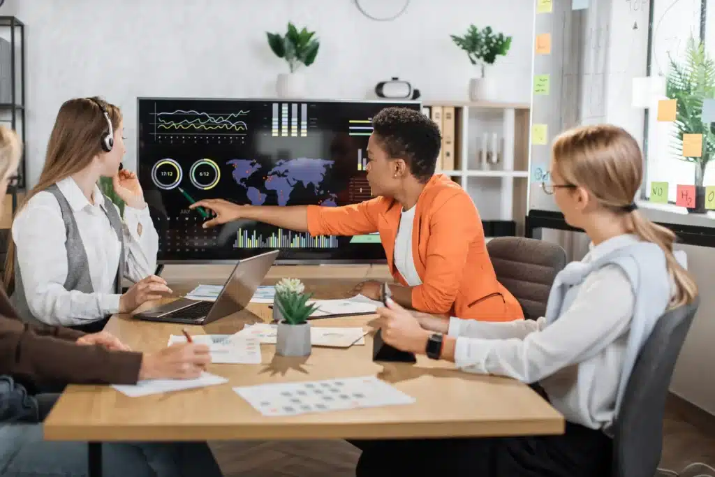 A digital web agency team reviewing data and analytics on a large screen while discussing strategy in a meeting room.