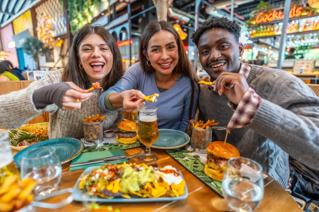 Group of friends enjoying burgers, fries, and nachos, demonstrating restaurant advertising ideas that promote menu highlights and social dining.