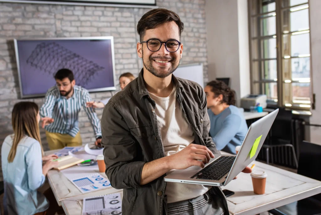 Marketing professional smiling while holding a laptop in a collaborative workspace, representing a trusted local SEO service provider.
