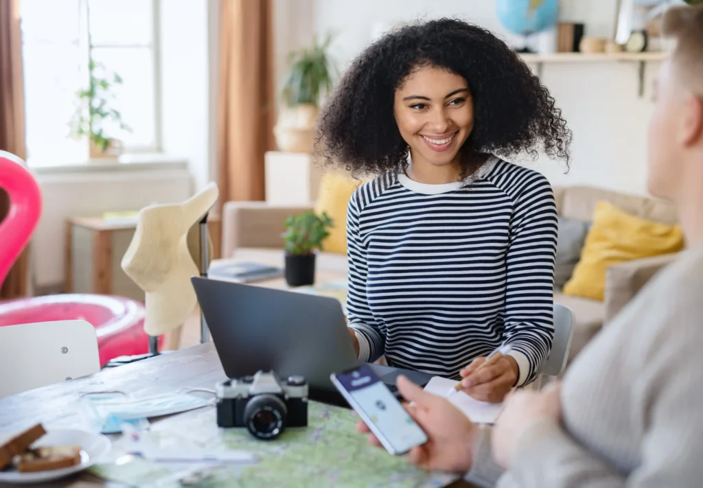Young woman smiling while using a laptop and discussing plans with a partner, illustrating collaboration and planning through freelance digital marketing services.