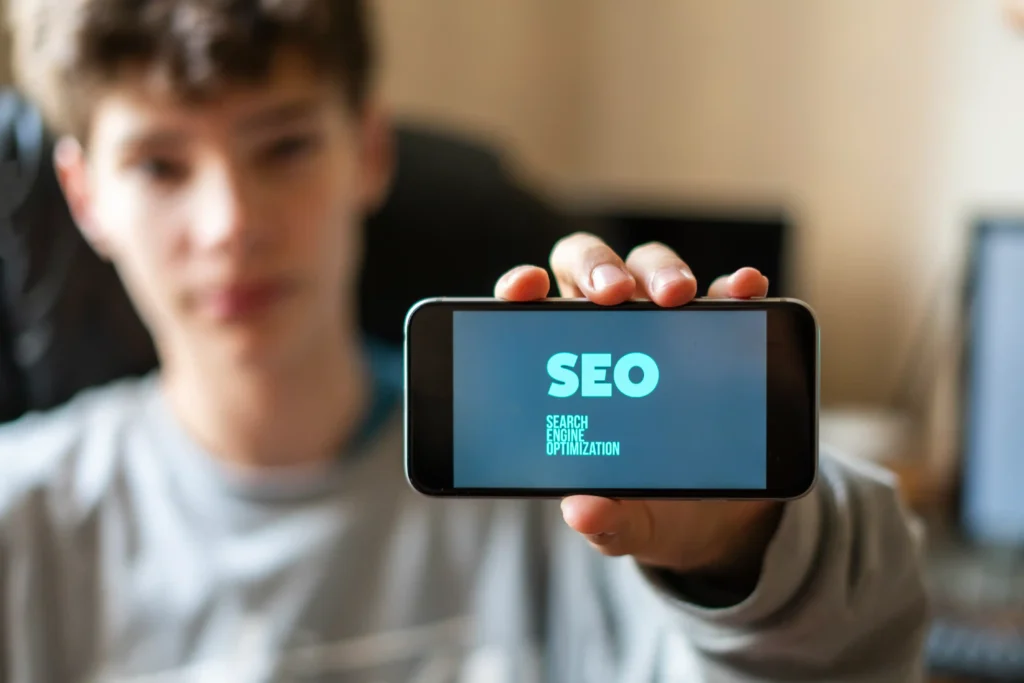 A young man holding a smartphone displaying the word SEO, illustrating mobile-friendly strategies in seo local services.